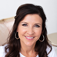A woman with shoulder-length brown hair, wearing hoop earrings and a black top designed with graphic design FAQs, smiling at the camera.