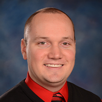 A portrait of a smiling man wearing a red shirt with a matching striped tie, garnering positive reviews.