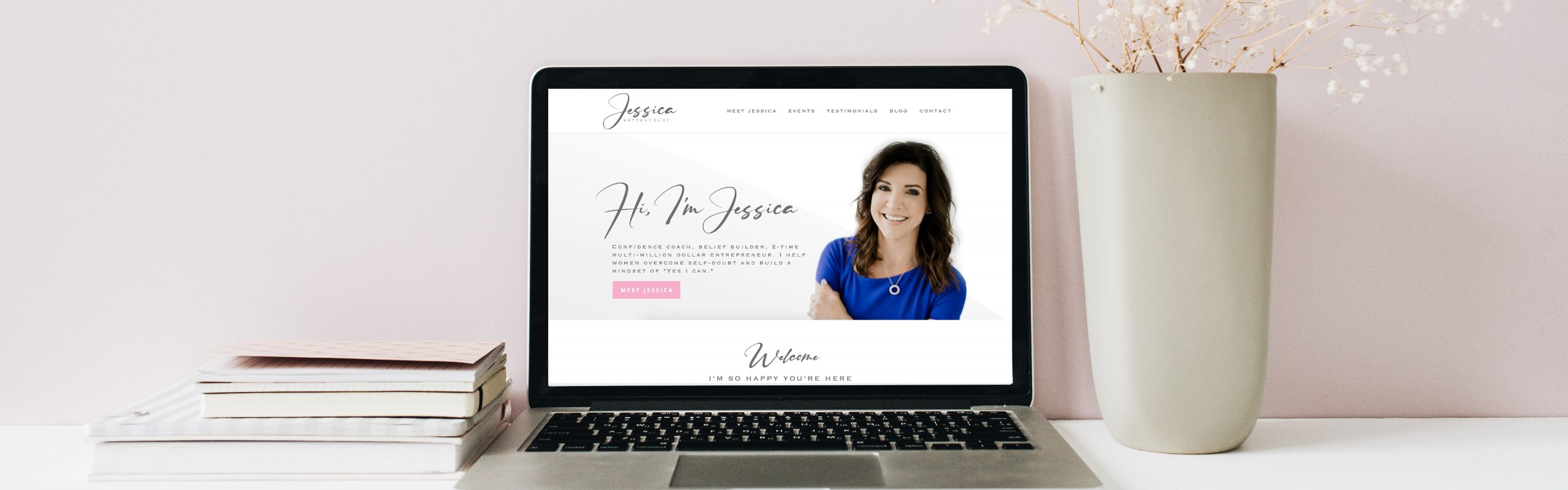 A laptop is open on a desk displaying Jessica Bettencourt's personal website with a photo of a smiling woman, accompanied by decorative elements such as a vase with branches and a stack of books, all
