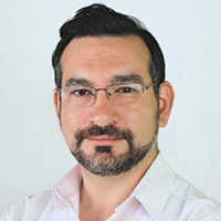 A man with facial hair and glasses wearing a white shirt, posing for a headshot against a light framework security background.
