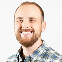 A man with a beard smiles at the camera, wearing a plaid shirt with positive reviews on a white background.