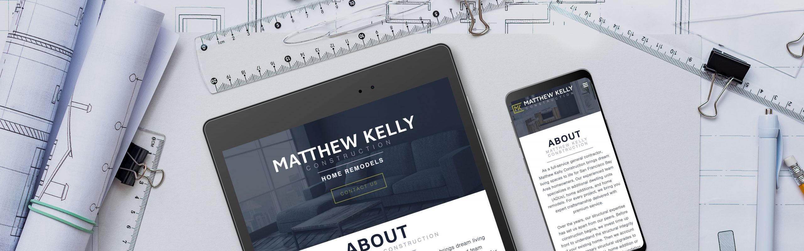 A tablet and smartphone displaying a construction company's website, overlaid on architectural blueprints and drafting tools.