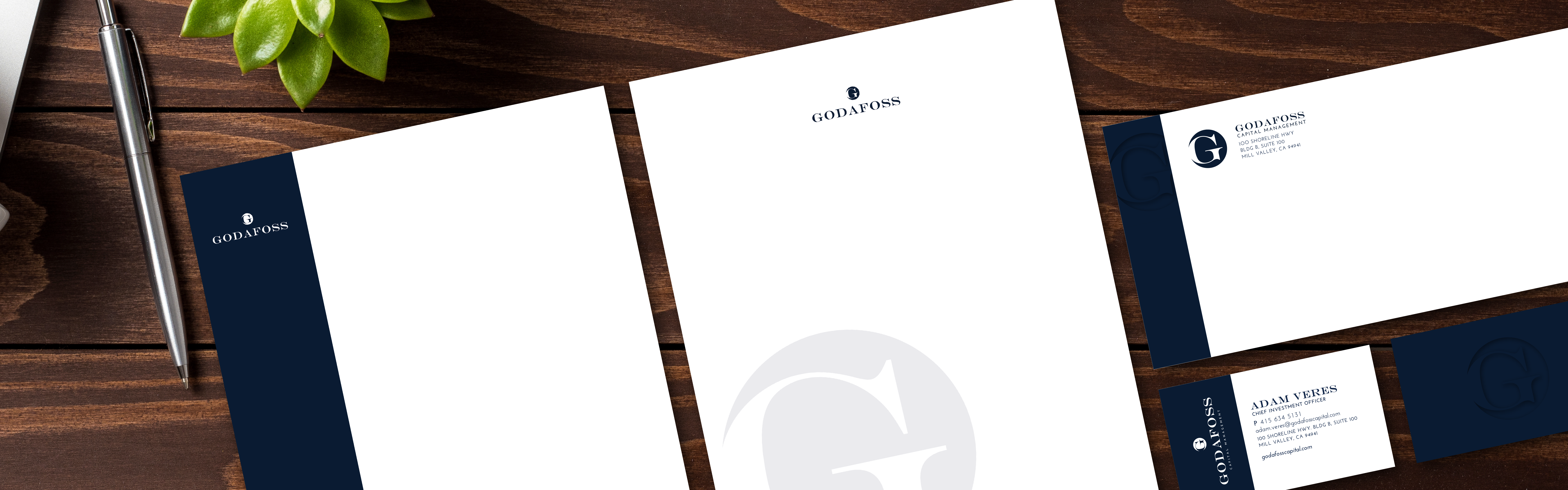 Corporate stationery set for Godafoss Capital Management including letterhead, business cards, and envelopes placed neatly on a wooden desk surface with a pen and a decorative plant.