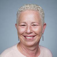 A portrait of a smiling woman with short, curly white hair, wearing earrings and a pink top against a blue-grey background, has garnered rave reviews.