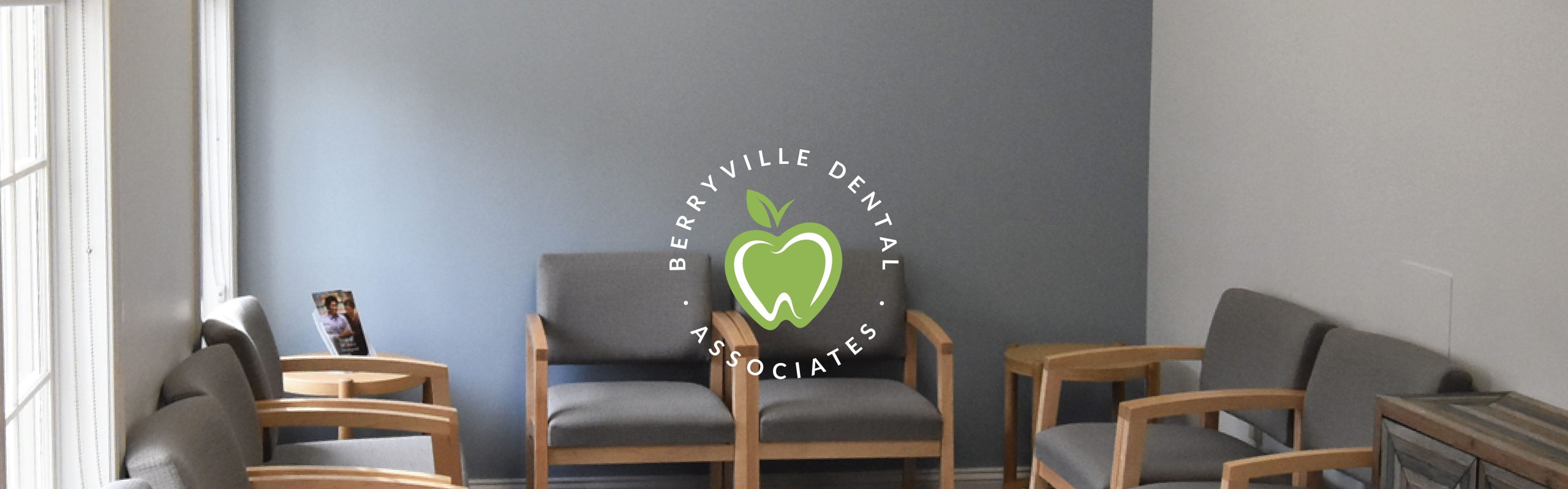 A tidy dental office waiting room with wooden chairs, a side table with magazines, and Berryville Dental Associates' sign on the wall.