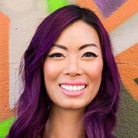 Woman with purple hair smiling against a colorful graffiti background, earning rave reviews for her vibrant look.